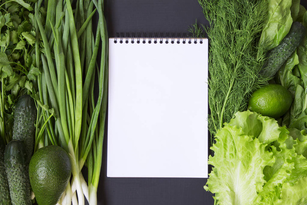 Green vegetables and fruits background (avocado, lime, cabbage, parsley, cucumber, dill, onion ,salad, spinach) with notebook. Top view. Flat lay. From above. Copy space. - Photo, Image