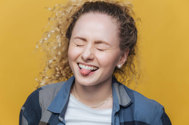 Фото смішної насолодженої жінки розважається наодинці, радісно сміється і показує язик, тримає очі закритими, виражає божевілля, ізольовані на жовтому тлі. Концепція людей та виразів обличчя
 - Фото, зображення