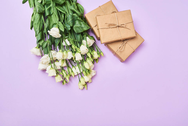 Ευχετήρια κάρτα με λευκό eustoma λουλούδια άνοιξη και η μικροσκοπική συσκευασία δώρου σε μοβ φόντο, χώρο για το κείμενό σας. το Top view - Φωτογραφία, εικόνα
