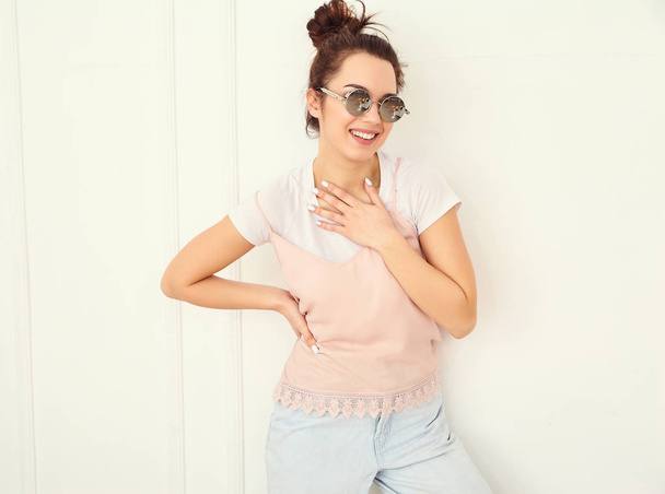 Portrait of young beautiful brunette woman girl model with nude makeup in colorful summer pink hipster clothes in sunglasses posing near wall. Going crazy and looking happily in camera  - Фото, изображение