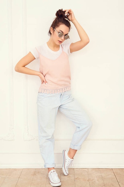 Portrait of young beautiful brunette woman girl model with nude makeup in colorful summer pink hipster clothes in sunglasses posing near wall. Full length - 写真・画像