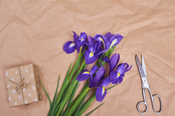 Biglietto di auguri con fiori di iris viola primaverili e scatola regalo su sfondo di carta marrone, spazio per il testo. vista dall'alto
 - Foto, immagini