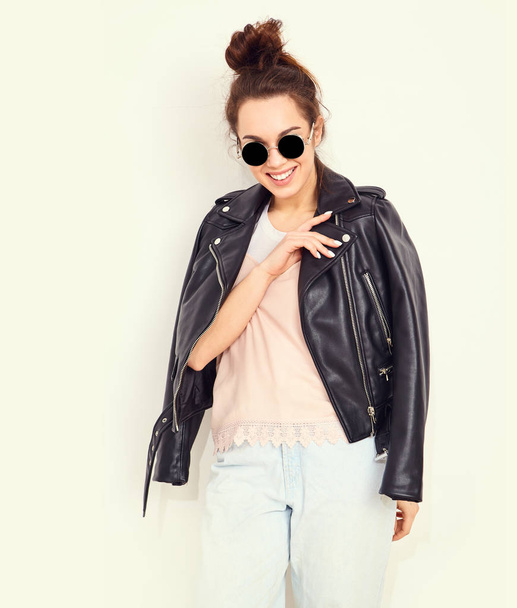 Portrait of young beautiful brunette woman girl model with nude makeup wearing summer hipster biker leather jacket clothes in sunglasses posing near wall. Going crazy  - Photo, Image