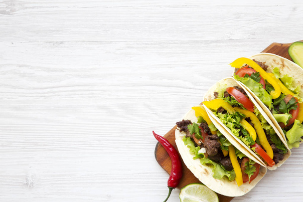 Tacos with pork, fresh vegetables, avocado, lime and pepper. White wooden background. Top view, flat, overhead. Copy space. - Photo, Image