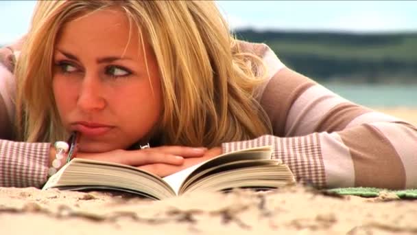 Beautiful young blonde girl reading on the beach - Video