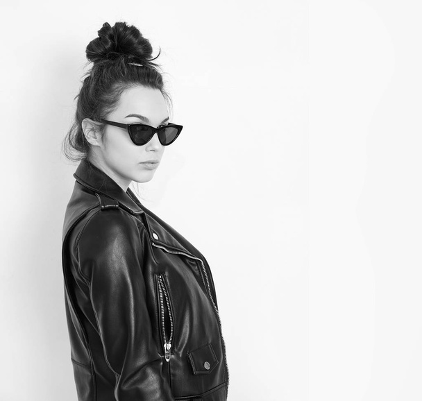 Portrait of young beautiful brunette woman girl model with nude makeup wearing summer hipster biker leather jacket clothes in sunglasses posing near wall. Going crazy  - 写真・画像