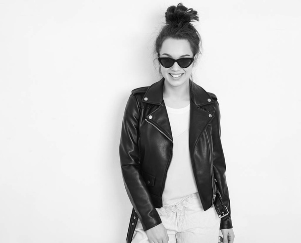 Portrait of young beautiful brunette woman girl model with nude makeup wearing summer hipster biker leather jacket clothes in sunglasses posing near wall. Going crazy  - Foto, immagini
