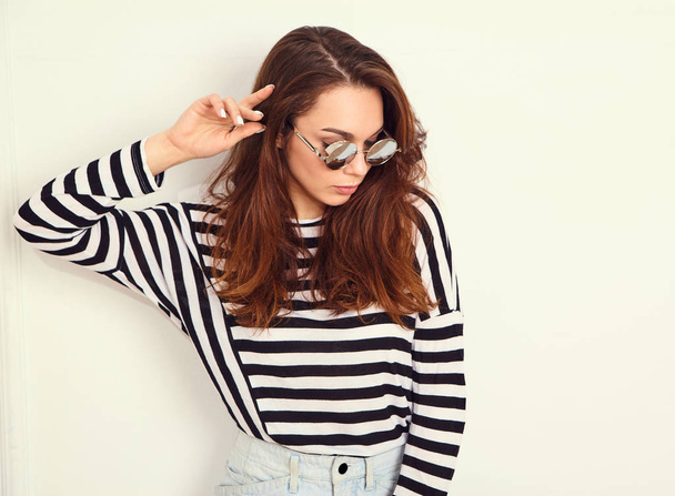 Portrait of young beautiful brunette woman girl model with nude makeup in summer hipster clothes and sunglasses posing near wall. Going crazy  - Zdjęcie, obraz