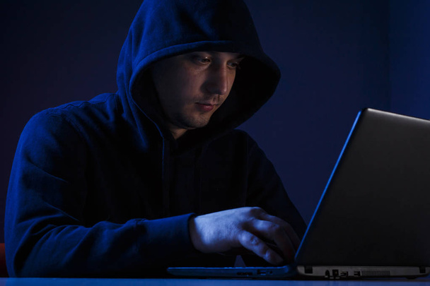 A young man in a hood behind a laptop - Fotó, kép