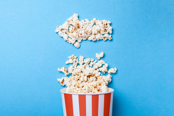 verschüttetes Popcorn in Form eines Pfeils nach links und Papiereimer in rotem Streifen auf blauem Hintergrund. - Foto, Bild