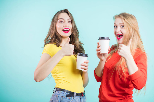 Happy smiling young two women with coffee cups giving a thumbs up gesture - Zdjęcie, obraz