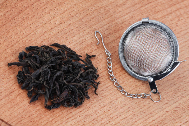 Tè nero, e colino da tè con catena, su sfondo di legno
. - Foto, immagini