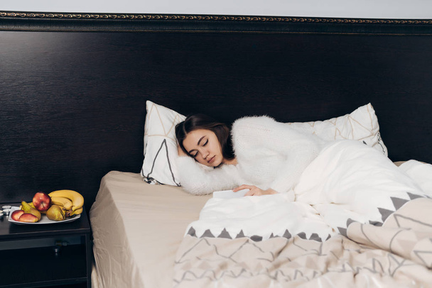 cute young girl in white pajamas sleeps on the bed early in the morning, does not want to get up - Fotografie, Obrázek