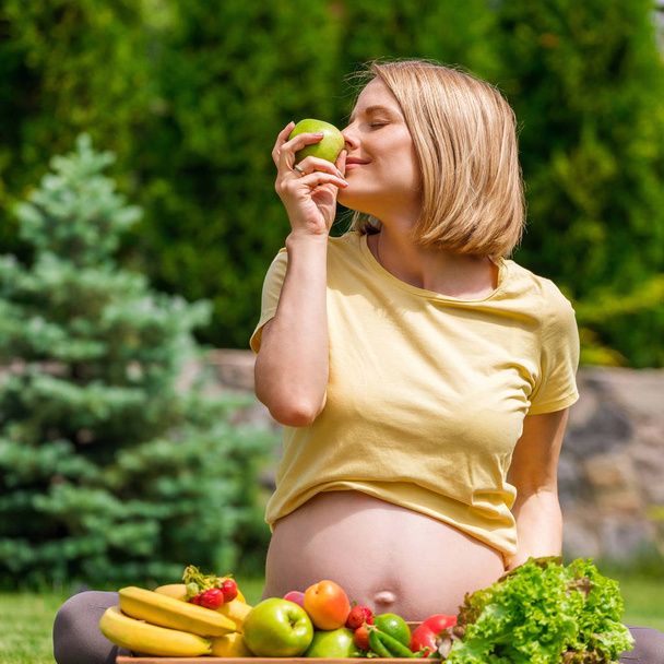 Pregnant woman sitting on grass and holding an apple in hand - 写真・画像