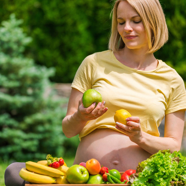 Pregnant woman sitting on grass and holding an apple in hand - Photo, image