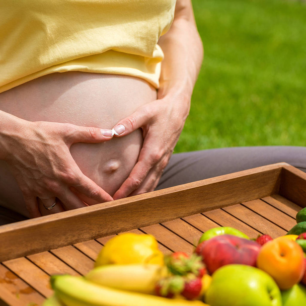 Pregnant woman sitting on grass and holding an apple in hand - Foto, Imagem
