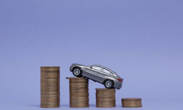 A gray model of a car with coins in the form of a histogram on a purple background. Concept of lending, savings, insurance - Fotografie, Obrázek