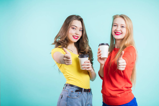 Happy smiling young women with coffee cups giving a thumbs up gesture. Positive emotions, communication, life style of the - Photo, Image