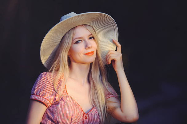 Kaunis nuori nainen vaaleanpunainen pilkullinen kesämekko ja aurinko hattu osoittaa kopioida tilaa, katsot kameraa. Kolme neljäsosaa studion pituudesta kuvattu tummalla luonnollisella taustalla
 - Valokuva, kuva