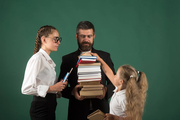 Teacher man and girls hold book pile at school. School time of sisters and father in library. Education in knowledge day. Literature lesson and reading grammar book. Back to school and home schooling. - Foto, Bild