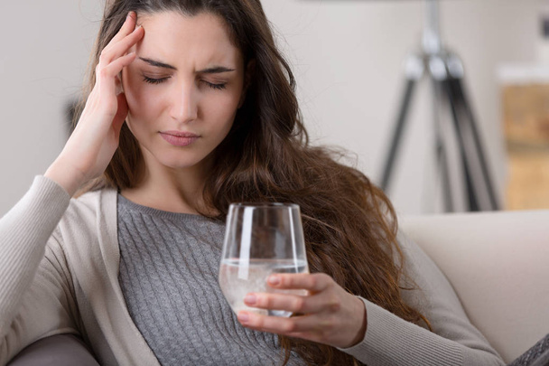Päänsärky Nainen ottaa pillerin lasillisella vettä
 - Valokuva, kuva