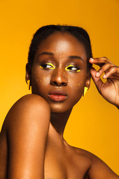 Cheerful young african woman with yellow makeup on her eyes. Female model laughing against yellow background. - Zdjęcie, obraz
