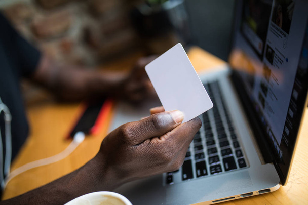 Close up of afro american man hands with white blank card for adv copy space in front of laptop and table background - 写真・画像