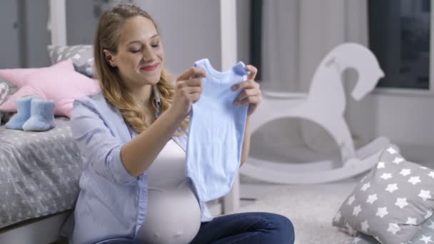 Smiling expecting woman holding newborn onesie - Imágenes, Vídeo