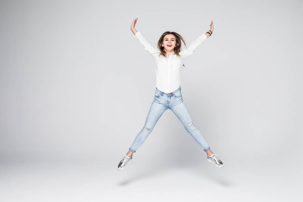happiness, freedom, power, motion and people concept - smiling young woman jumping in air with raised fists over white background - 写真・画像