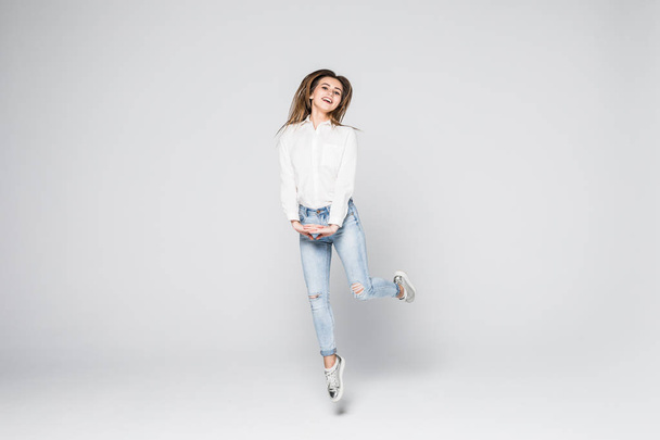 Joyful moments. Full length portrait of a young beautiful brunette girl jumping and smiling happily isolated on white background - Zdjęcie, obraz