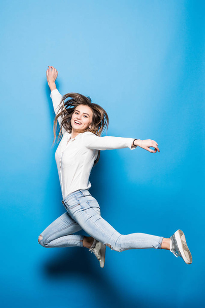 happiness, freedom, power, motion and people concept - smiling young woman jumping in air with raised fists over blue background - Foto, afbeelding