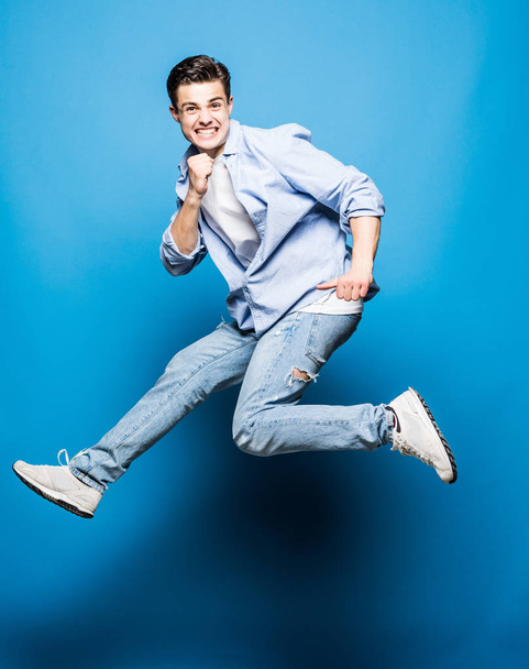 glücklich aufgeregt fröhlicher junger Mann springt und feiert Erfolg isoliert auf blauem Hintergrund - Foto, Bild