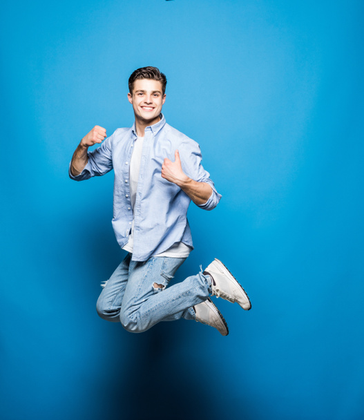 Knappe man springen geïsoleerd op blauwe achtergrond - Foto, afbeelding