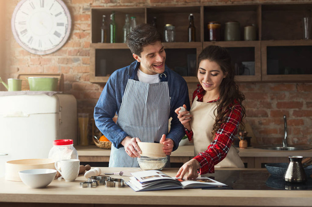 Happy young woman and man baking in loft kitchen - Фото, изображение