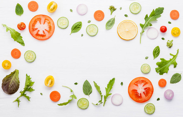 Food pattern with raw ingredients of salad, lettuce leaves, cucumbers, tomatoes, carrots, broccoli, basil ,onion and lemon flat lay on white wooden background. - Photo, Image