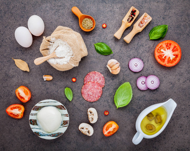 The ingredients for homemade pizza with ingredients sweet basil ,tomato ,garlic ,bay leaves ,pepper ,onion and mozzarella cheese on dark stone background with flat lay. - Фото, зображення