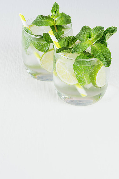 Fresh spring drink with slices lime, twig mint, ice, bubbled water, straw on soft blue wood plank, top view, copy space. - Photo, Image