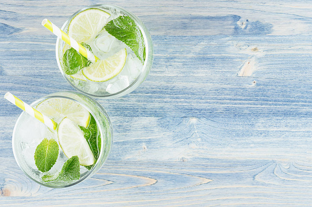Fresh cold summer beverage mojito with lime, leaf mint, straw, ice cubes, soda on blue wood background, top view, border. - Fotoğraf, Görsel