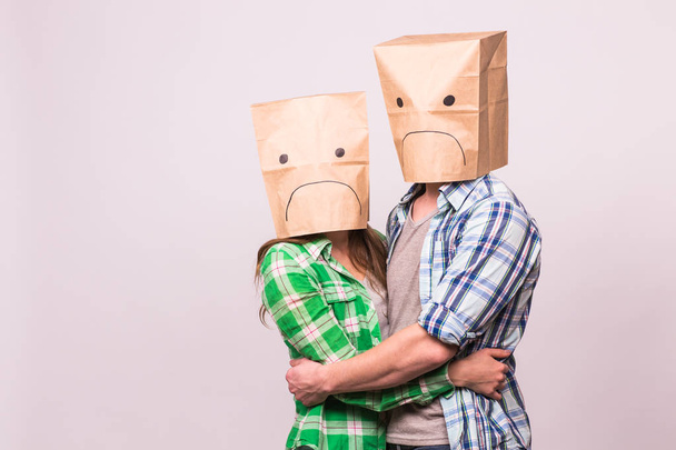 love, family and relationship problems concept - unhappy couple covering their sad faces with paper bag over white background. - Photo, Image
