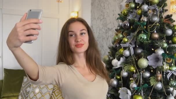 Slow motion teacher girl taking selfies near New Year tree using smartphone. - Footage, Video