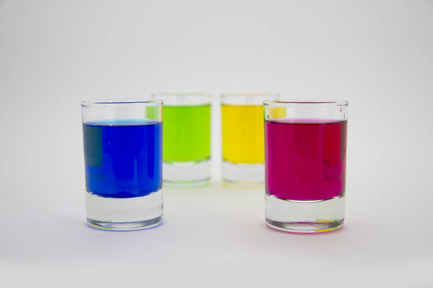 Multicolored glasses of different drinks. Party and holiday celebration concept. Four glasses with a blue, green, yellow and red drink. Isolated on white background. - Foto, afbeelding