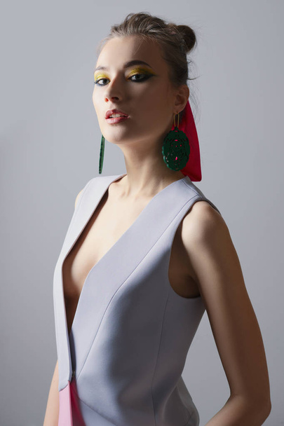 Portrait of beautiful fashion model in sleeveless jacket. Bright makeup and big earrings - Фото, изображение