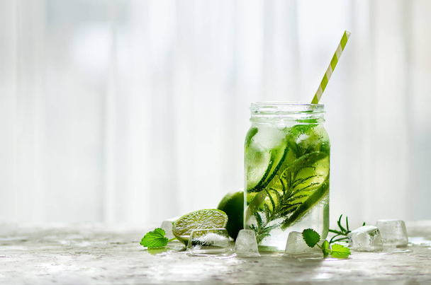 Cold and refreshing detox water with lime, cucumber, rosemary and ice in glass jar. Copyspace. - Foto, Imagen