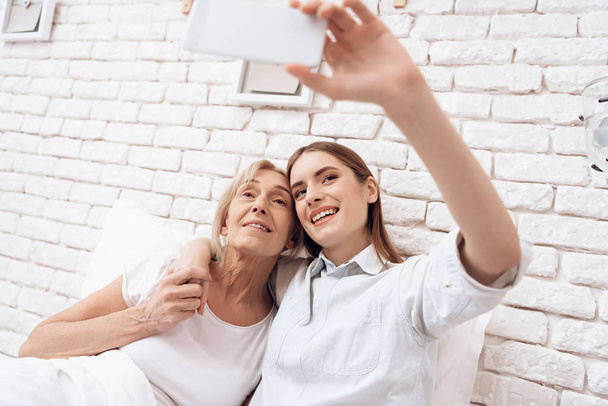 Yatakta ve alma selfie smartphone cep telefonu ile Hemşirelik yaşlı kadın kız - Fotoğraf, Görsel