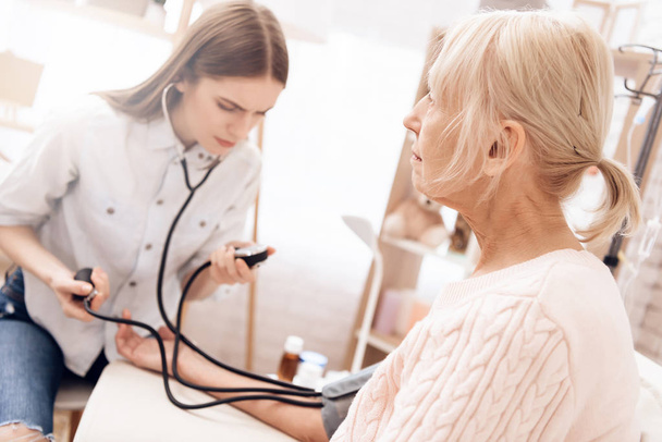 Girl nursing elderly woman and using tonometer to measure blood pressure - Foto, Bild