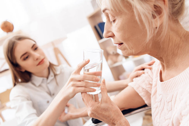 Girl caring for elderly woman and helping woman with glass of water - Foto, afbeelding
