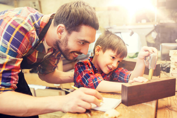 dad and son with ruler measuring plank at workshop - Foto, afbeelding