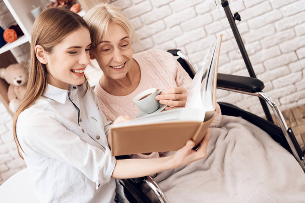 Girl nursing elderly woman, they looking pictures in photo album - Photo, image