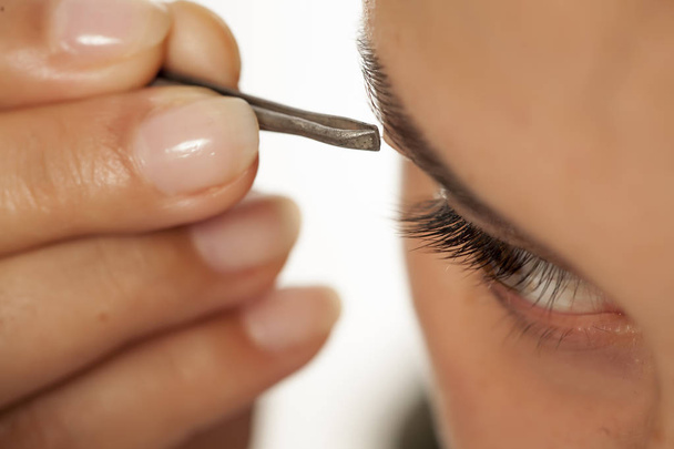Young beautiful woman plucking her eyebrows with tweezers - Photo, image
