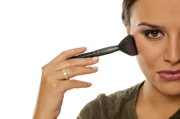 Beautiful young woman applying blush with a brush on a white background - Photo, Image